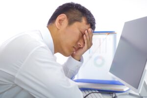 パソコン画面を見て頭を抱える男性